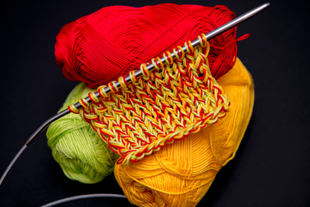 balls of yarn red green and yellow on a black background and knitting needlesの写真素材