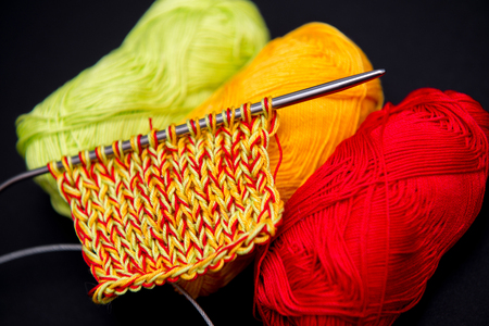 balls of yarn red green and yellow on a black background and knitting needles の写真素材