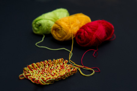 balls of yarn red green and yellow on a black background and knitting needlesの写真素材