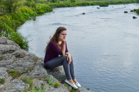 a young girl is sitting on a rock near the riverの写真素材