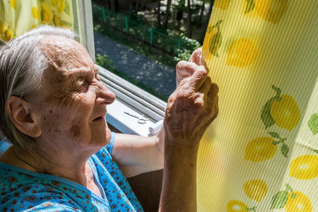 Chelyabinsk Russia july 16 2020 grandmother stitches a hole in the curtain on the balcony of an apartment buildingのeditorial素材