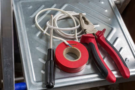 electrician's tools pliers and a screwdriver are on the sliding ladder