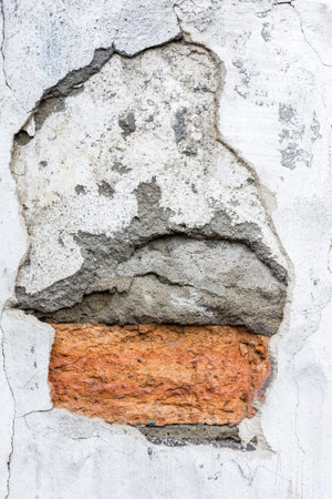 red brickwork under a layer of old crumbling plaster on the wall of the houseの写真素材