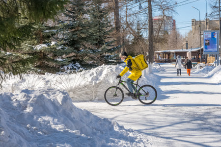 Chelyabinsk Russia 03 March 2021 a food delivery courier carries an order on a bicycle in a winter parkのeditorial素材