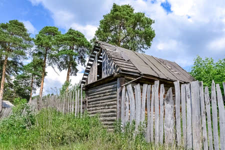 an abandoned barn and an old wooden fence stand on the edge of the village near the forestの写真素材