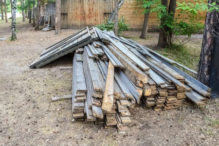 Old boards lie in a pile among the trees near the fence.