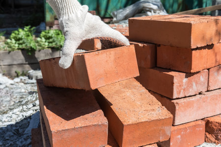 Construction work in the garden. A bricklayer takes a brick from a stack to build a barn wall.