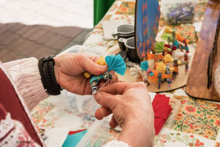 Master class on making handmade souvenirs. A woman makes a decorative doll-amulet.