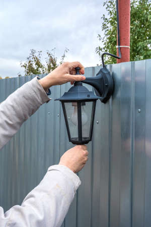 A gardener installs a street lamp on a metal fence. Household work in the garden.