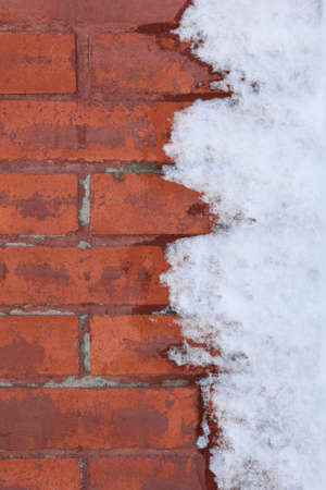 The old red brick wall is half covered with snow. Vertical background and texture of brickwork.の写真素材