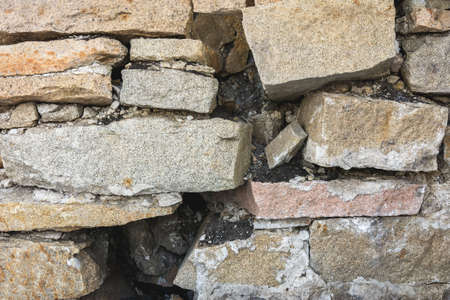 An ancient stone wall made of granite blocks is being destroyed by old age. The texture of natural stoneの写真素材