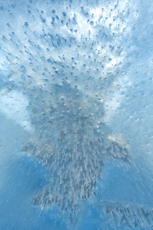 Air bubbles rising from the bottom froze in transparent blue ice. Ice pattern and texture.