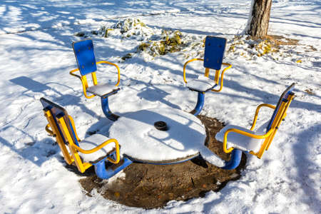 The snow-covered children's carousel melts in the bright sun. Urban landscape in a winter park.
