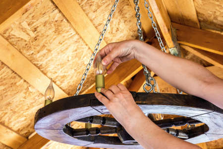 A woman replaces a light bulb on a chandelier in a summer gazebo in the garden. Household chores
