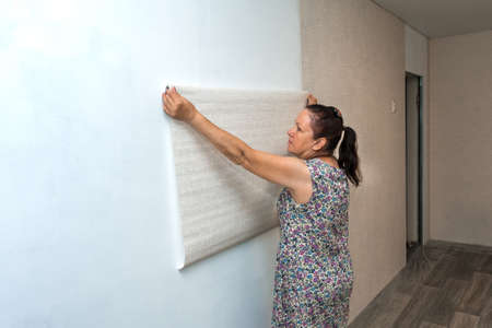 A female painter is pasting wallpaper on the wall. Renovation of residential premises