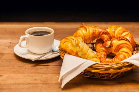 cup of coffee with croissant and a cake basket in the background. Stock imageの写真素材