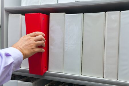 Man's hand taking off the shelf red folder with documents archive file stock photoの写真素材