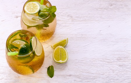 Fresh cocktail Mojito with dark rum ice lemon and mint on a light coloured wooden rustic tableの写真素材
