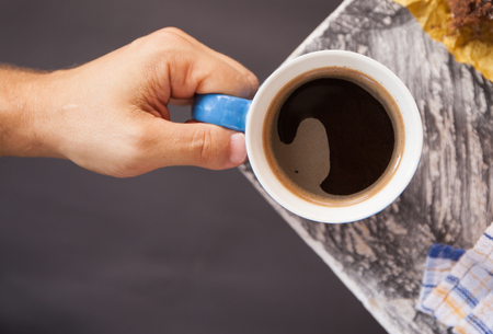 Cup of black coffeein male hand on the background of the wooden surface at the corner of the table. Flat layoutの写真素材