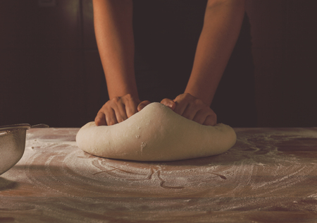 Making dough by female hands on a wooden baking table. Dark black background with flour. Side view, horizontal photoの写真素材