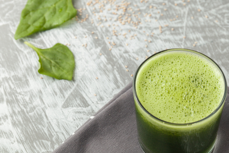 Fresh green spinach smoothie in a glass cup on a gray wooden surface. Flat layoutの写真素材
