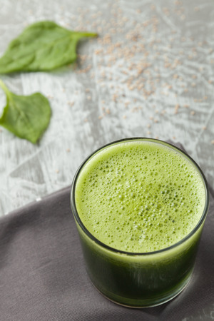 Fresh green spinach smoothie in a glass cup on a gray wooden surface. Flat layoutの写真素材