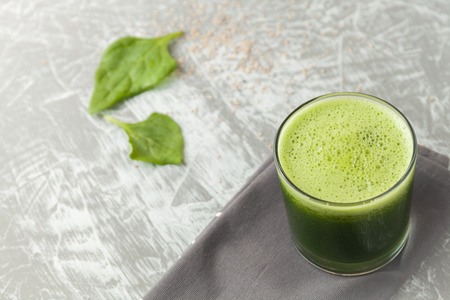 Fresh green spinach smoothie in a glass cup on a gray wooden surface. Flat layoutの写真素材