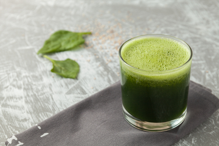 Fresh green spinach smoothie in a glass cup on a gray wooden surface. Flat layoutの写真素材
