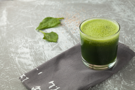 Fresh green spinach smoothie in a glass cup on a gray wooden surface. Flat layoutの写真素材