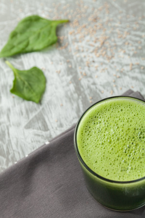 Fresh green spinach smoothie in a glass cup on a gray wooden surface. Flat layoutの写真素材