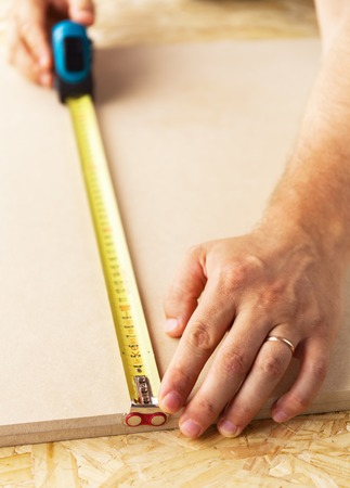 Yellow Measuring Tape in the hands of an experienced carpenter at workの写真素材