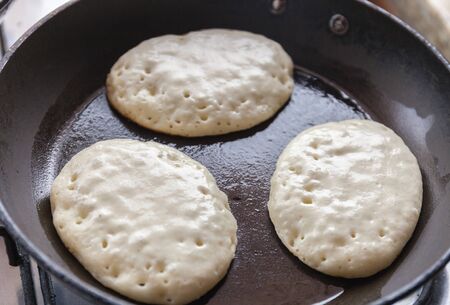 Cooking pancakes on the halfway in a pan with butter as delicious breakfast meal for a happy familyの写真素材