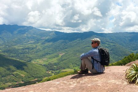 Tourist man sits on a cliff edge on the top of mountain with gorgeous view at stunning valley in the subtropical part of Bolivia. Samaipataの写真素材