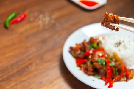A slice of hot chicken on chopsticks. Sweet and Sour Chicken on Rice. Typical Asian dish. A lot of negative space for text. Stock photoの写真素材