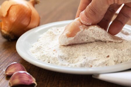 Breading of raw chicken. Hand lift a piece of fillet out of flour with spices. close up shot. onion garlicの写真素材