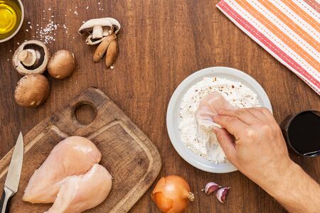 Raw fillet. Cooking Chicken. Breading with flourby hand, starch and spices. Lemon, fresh champignons, onions, garlic, wine, salt and olive oil. Wooden cutting board. Top layoutの写真素材