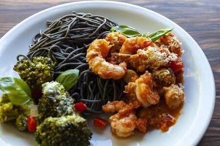 Black spaghetti with shrimp tomato sauce and baked broccoli with Roquefort cheeseの写真素材