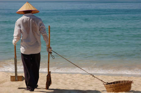 Vietnamese garbage collector at Nha Trang beach. Uses a scoop, broom and waste basket. Vietnam.の写真素材