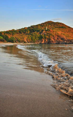 Waves of a sandy beach against a background of mountains and blue sky. Blur the foreground.