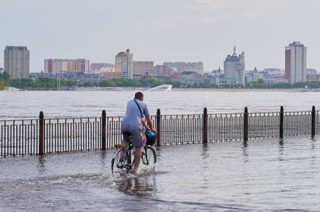 Blagoveshchensk, Russia - June 21, 2021: Father and child ride a bicycle along a flooded city embankment. Flood of the Amur River. Natural disaster.の写真素材
