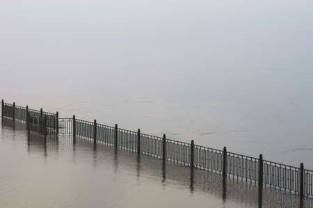 The fence of the city embankment during flooding with water and fog. Geometrically straight line....