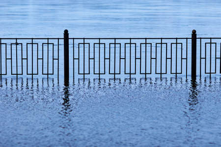 A metal fence of a flooded embankment with reflections. Selective focus on the geometric grid.