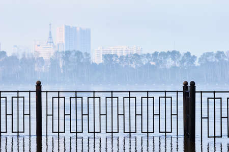Fence of the city embankment during flooding with water. Very heavy fog. Colorless early morning before sunrise.の写真素材