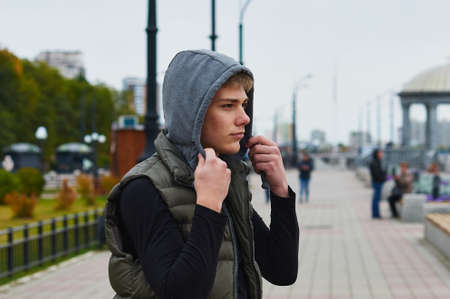 Young man in a hood on the embankment. Rotunda and street lamps. Acne on the face. Blur the background.の写真素材