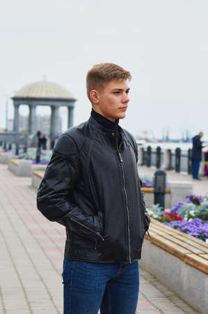 Handsome brutal man in black leather jacket model style. Portrait of a handsome guy on a blurred urban background with a rotunda.の写真素材