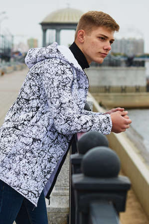 Portrait of a young handsome man in a black and white fashionable jacket on the city embankment against the background of the rotunda. Skin acne. Selective focus.の写真素材