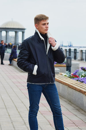 A guy in a warm leather jacket on the embankment with a rotunda is holding his collar. Selective focus.の写真素材