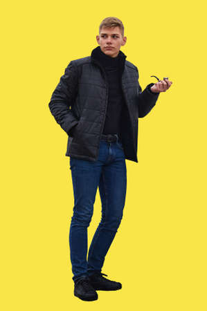 Young man in jeans and leather jacket on isolated illuminating yellow background. Tobacco pipe in...