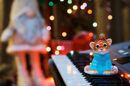 2022. Year of the tiger. Happy Chinese New Year. Christmas tree toy on the piano keys. Colored lights of an electric garland and a silhouette of a gnome in blur. Musical instrument. Selective focus.の写真素材