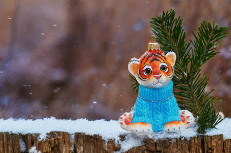 Tiger cub with Christmas tree toy outdoors. Snowflakes are falling. Blurred background. Merry Christmas. The symbol of the new year 2022.の写真素材